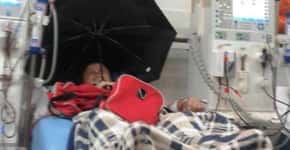 Idoso se protege de goteira com guarda-chuva em hospital