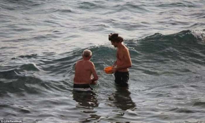 Avô e pai tiram a criança do mar após o parto