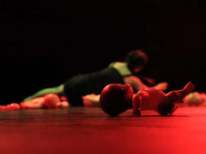 Foto do espetáculo “Con La boca bien abierta”, em que uma bailarina e diversas bonecas estão deitados no palco