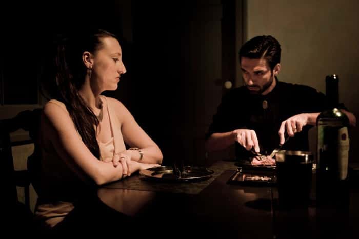 Dois atores sentados em uma mesa comendo