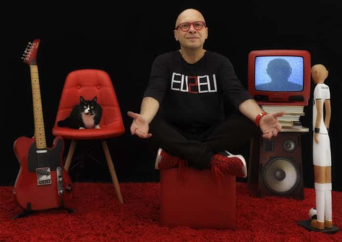 Fernando Salem em um cenário com uma cadeira, uma TV e um som