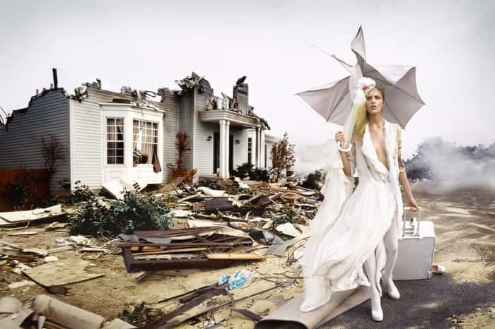 Mulher com vestido branco na frente de casa destruída