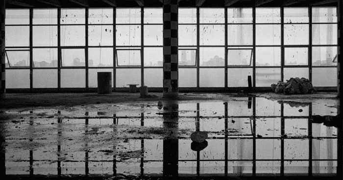 Foto em preto e btanco mostrando uma janela de vidro e uma grande poça de água do lado de fora