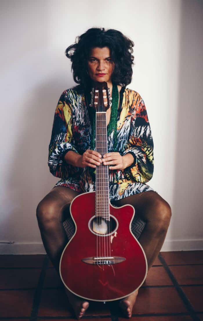Foto de Déa Trancoso sentada segurando um violão vermelho