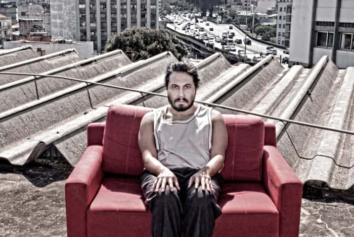 Ator Fernando Aveiro sentado em um sofá vermelho