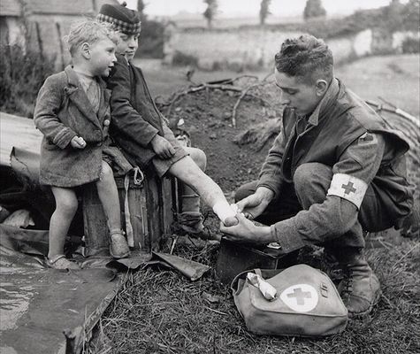 Um médico enfaixa o pé ferido de uma criança, enquanto seu irmão mais novo olhar sobre. [II Guerra Mundial de 1944]