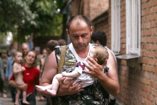 Um policial russo carrega um bebê liberado da escola em poder de homens e mulheres mascarados fortemente armados, na cidade de Beslan. [2004]