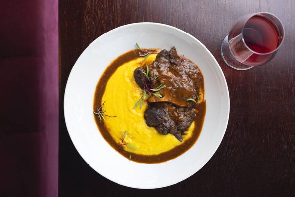 Polenta Cremosa com Ossobuco alla Milanese (R$119), preparada lentamente com manteiga e parmesão, servida com ossobuco bovino cozido por horas em vinho