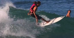 Pai surfista leva a filha nas costas para pegar onda