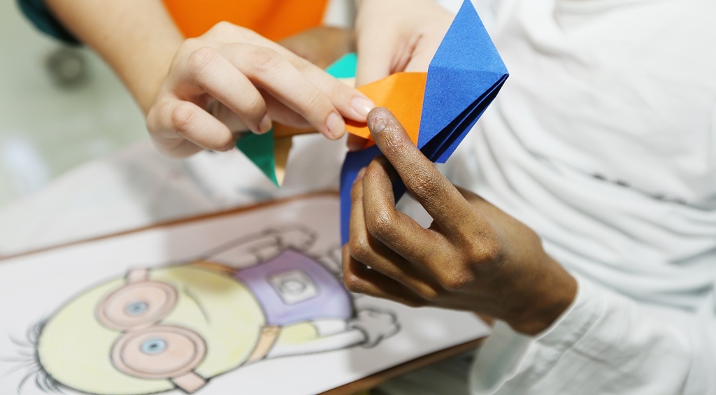 Mãos de paciente e voluntário criam origami de papel