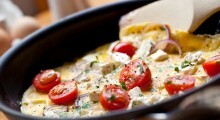 Cooking omelet in a pan, ready to serve.  With Cherry tomatoes, red onion, goat's cheese and parsley.  Shallow DOF.