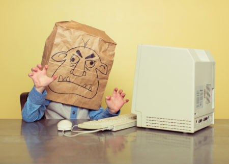 pessoa com um máscara de monstro e gestos agressivos na frente do computador