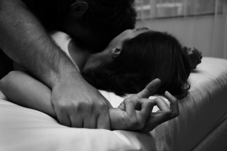 homem prendendo uma mulher na cama em simulação de estupro