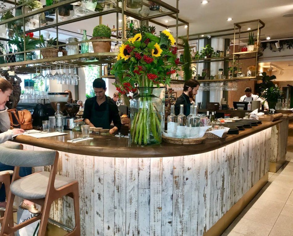 Mesas do Farmacy ficam ao lado do bar, cheio de plantas, no restaurante em Notting Hill. Passe a seta do post abaixo do Insta para ver