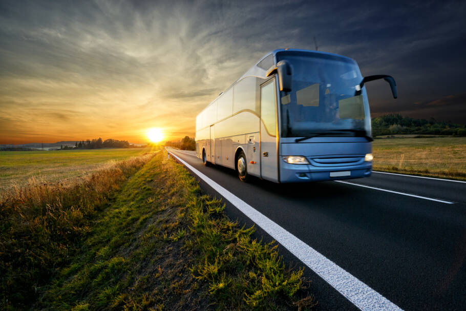 Bus traveling on the asphalt road in rural landscape at sunset