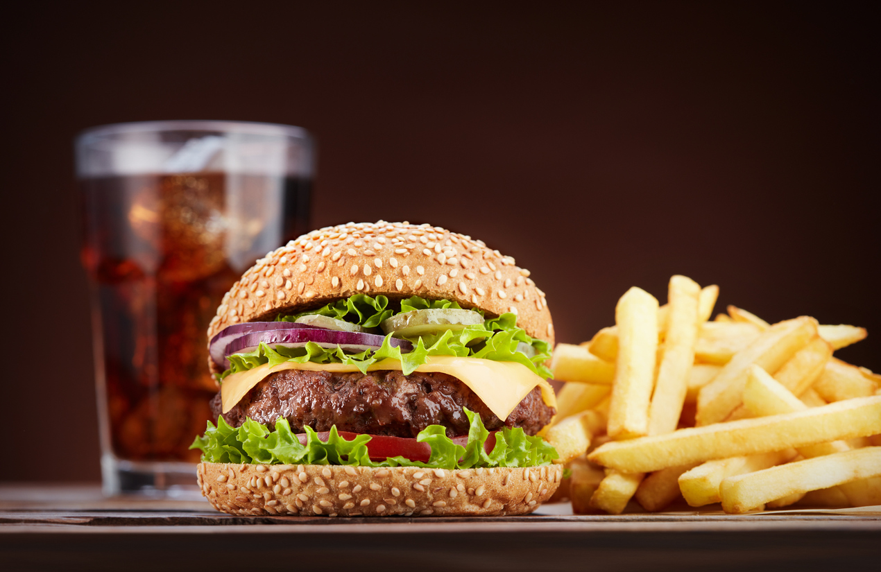 fresh cheeseburger with glass of cola and pile of french fries on wooden table