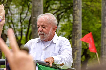 Foto mostra presidente Lula usando blusa social branca e indo discursar em um local aberto