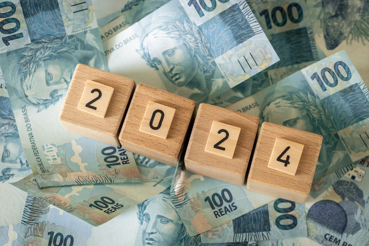 O ano de 2024 representado por quadrados de madeira em cima de várias notas de 100 reais