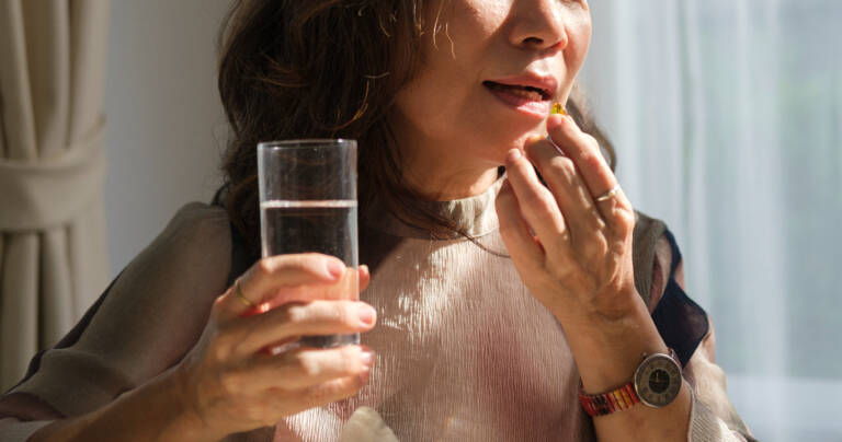 Mulher madura segurando pílula e copo de água, tomando suplemento de vitamina D