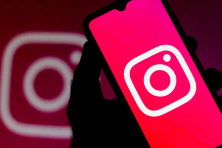 Pessoa segura celular com aplicativo do Instagram aberto e logomarca da rede social aparece ao fundo