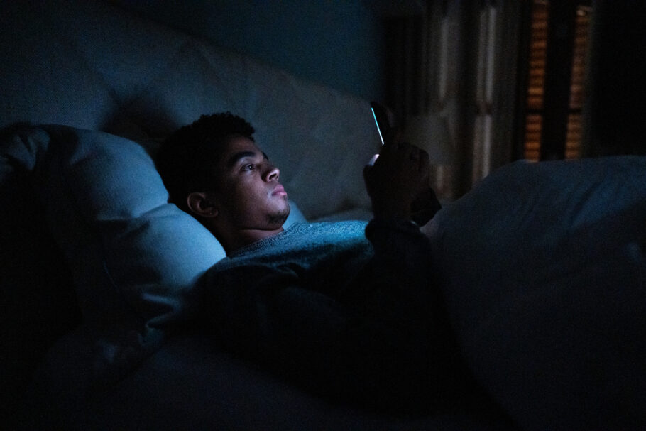 Young man using smartphone in bed at home