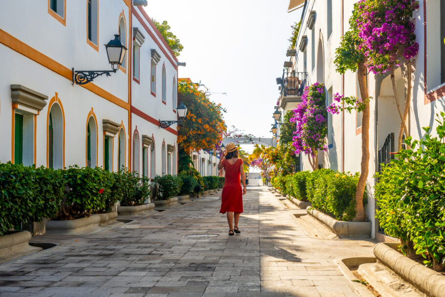 Uma mulher de vestido vermelho caminha por uma rua estreita em Cartagena, ladeada por árvores e prédios