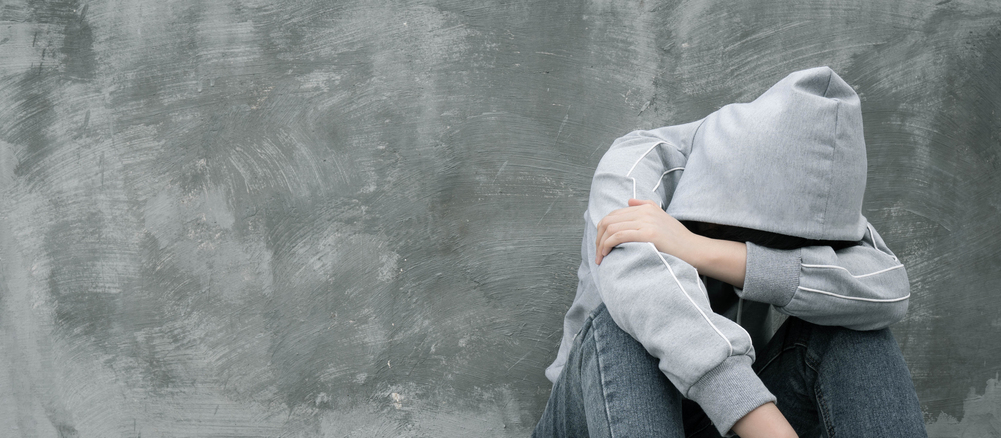 Depressed and hopeless teenage girl sitting alone after using drugs or drunk alcohol over grunge concrete wall. Drugs addiction and withdrawal symptoms concept. International Day against Drug Abuse.