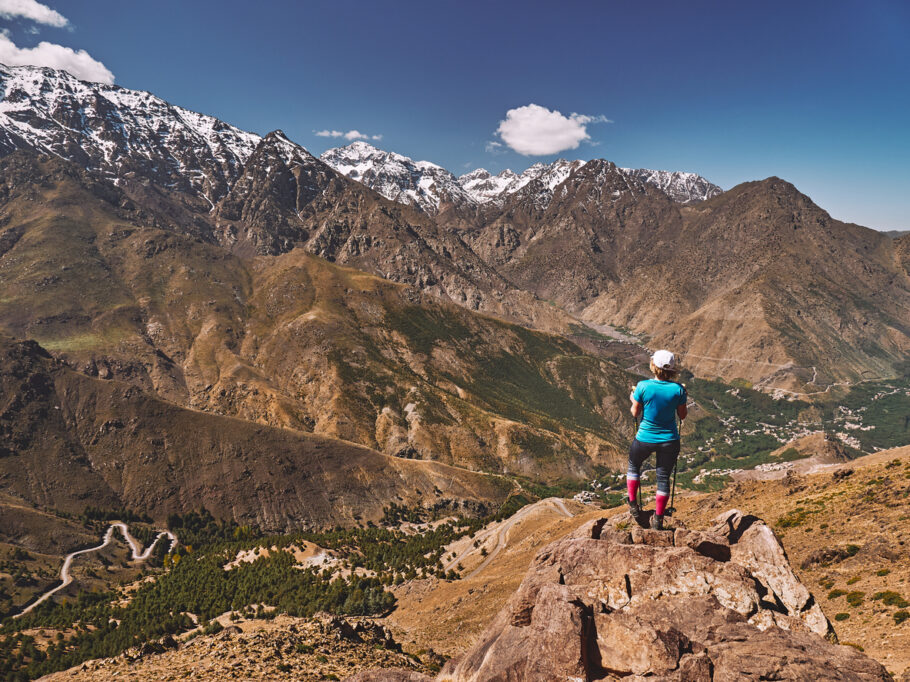 Turista loira caucasiana em uma caminhada olhando para os picos nevados das montanhas do Alto Atlas com Jebel Toubkal no meio em Marrocos, África