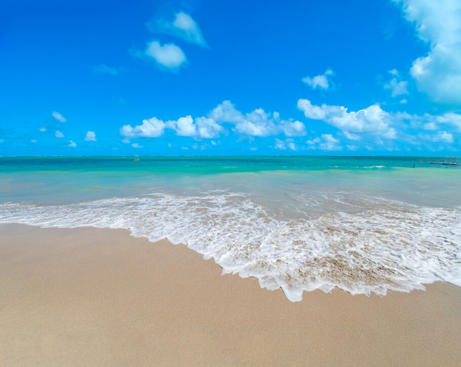 Linda paisagem com a água do mar batendo calmamente na areia da praia em tons de ciano em um lindo dia de céu azul. Praia de Barra Grande, Maragogi – AL, Brasil.