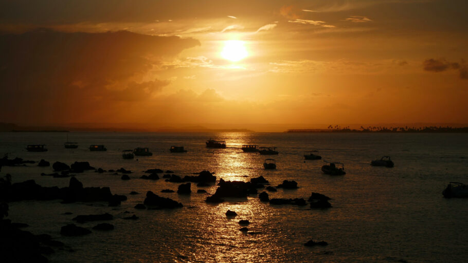 Um pôr do sol dourado cênico com a silhueta de rochas no mar no porto de Morro de São Paulo, Brasil