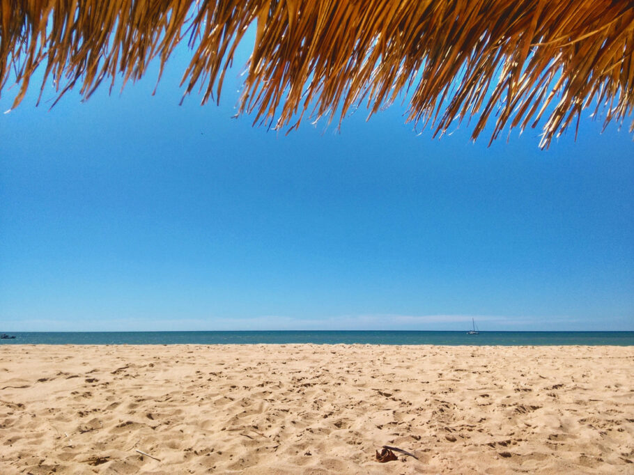 Telhado de palha. Horizonte sobre o mar. Areia e água do mar. Céu azul e limpo. São Miguel do Gostoso, Rio Grande do Norte, Brasil.