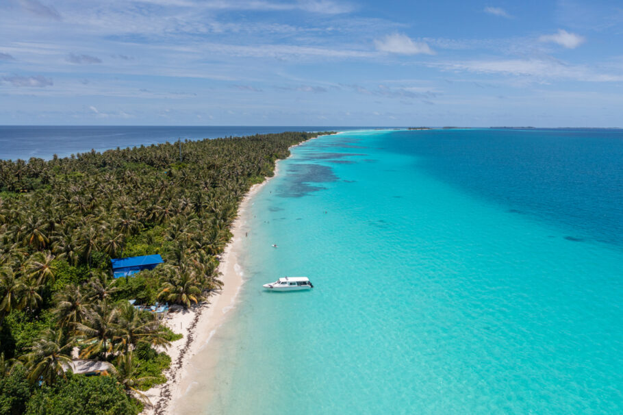 Ilha estreita no Oceano Índico nas Maldivas cercada por água azul vista aérea, Dhigurah