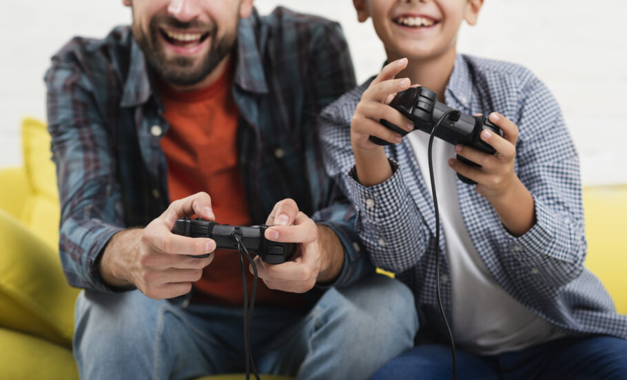 Pai e filho compartilham momentos de diversão e conexão enquanto jogam videogame juntos, mostrando como os games podem unir gerações.