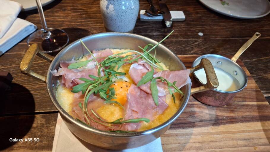 Polenta gratinada com gema de ovo caipira, presunto parma san danielle, mini rúcula e fonduta de parmesão