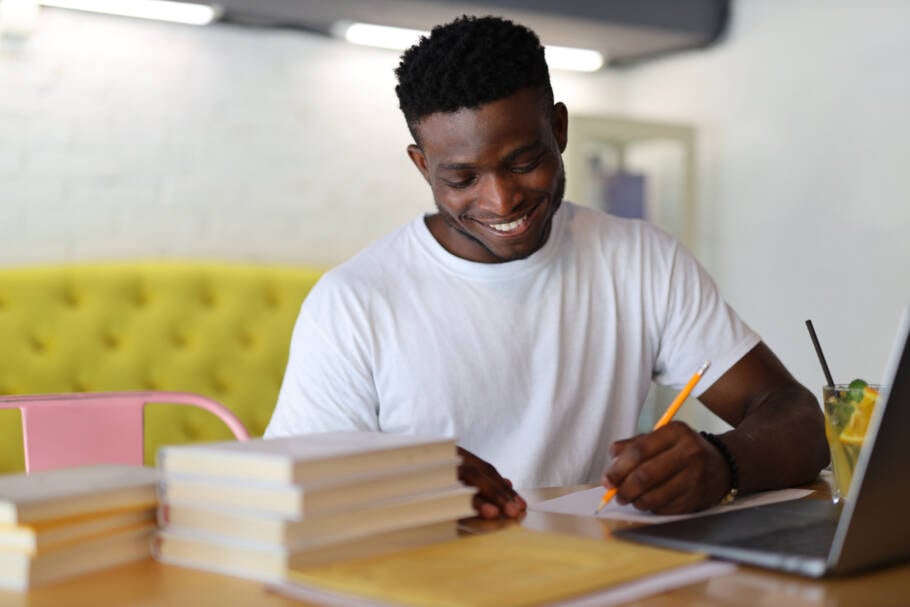 A focused African American student studying in a university library, surrounded by books and academic resources.