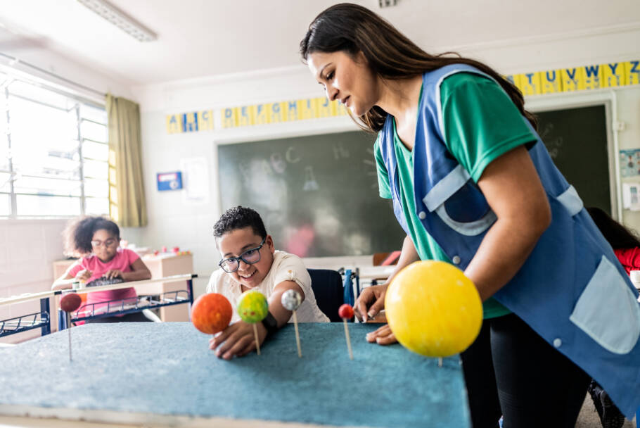 Teacher teaching wheelchair student on solar system project on classroom at school