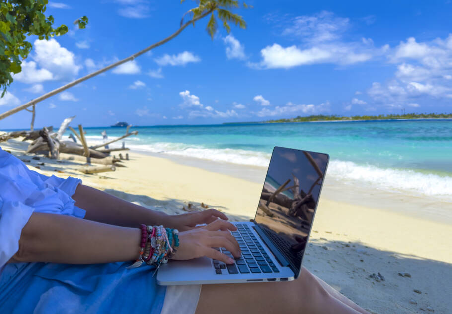 Nomad digital with laptop and running remotely with bright scenic view near poolside on the beach in summer time