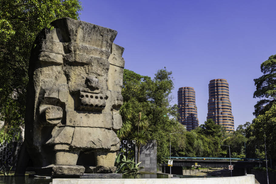 Estátua de pedra da deusa asteca Coyolxauhqui no Parque Chapultepec, com arranha-céus modernos ao fundo, na Cidade do México