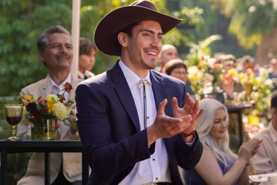 Protagonista de "O Babá", usando terno e chapéu marrom, sorrindo e aplaudindo