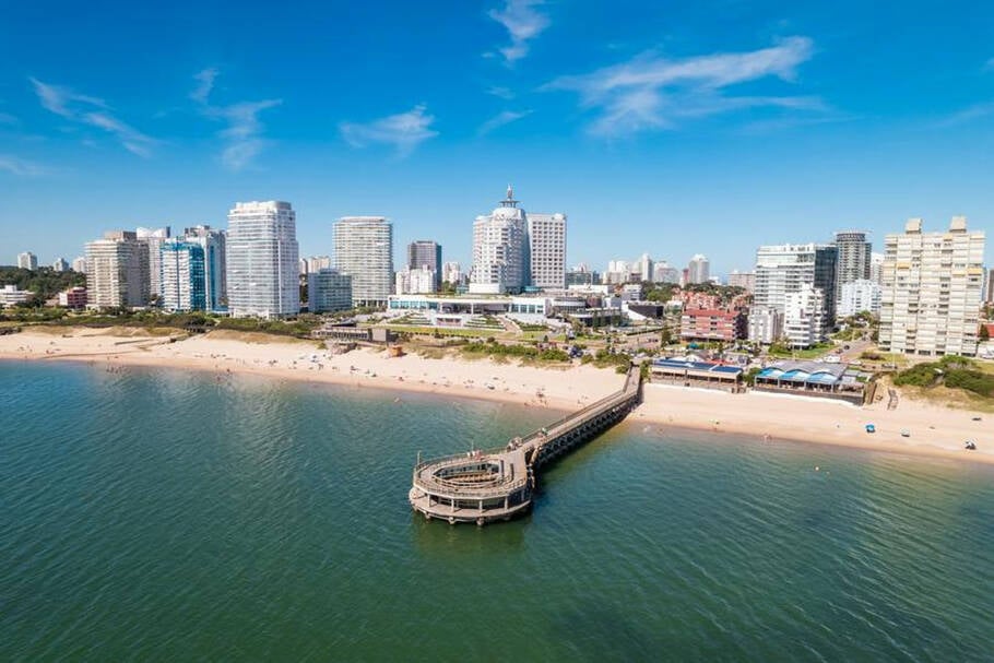 Aerial view of Punta del Este’s coastline with modern buildings and a pier under a clear blue sky.
