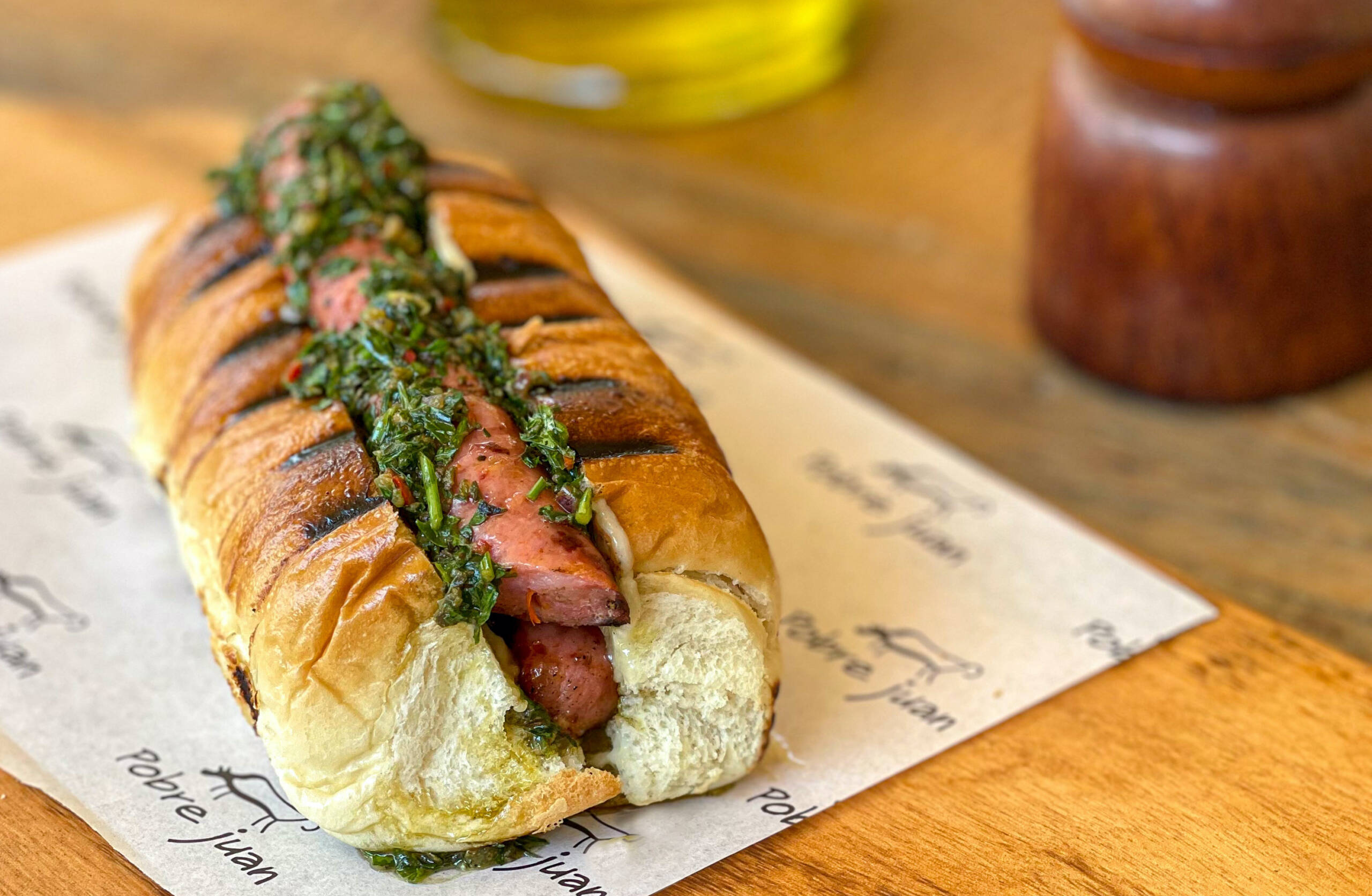 Servido no pão de batata, no Pobre Juan o choripán leva linguiça fininha de pernil, chimichurri e maionese temperada