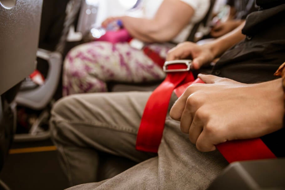 Passengers in an airplane cabin with their red seatbelts fastened. Close-up of traveler buckling seatbelt on a flight, highlighting airline safety