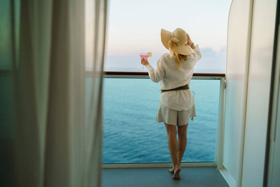 Rear view of carefree woman whit sun hat and cocktail on a balcony of a cruise ship
