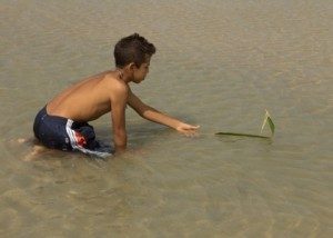 Folha de coqueiro vira barquinho nas mãos de menino.